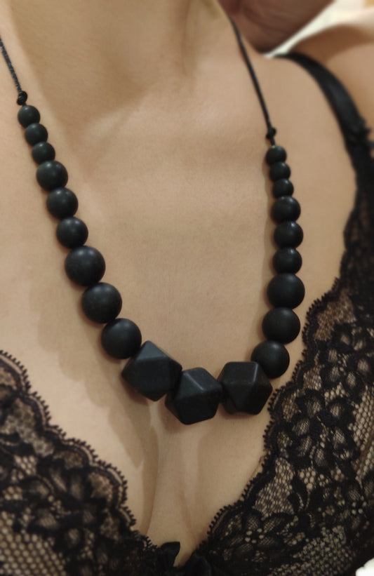 Collier de perles noires mates porté sur un décolleté, perles hexagonales au centre