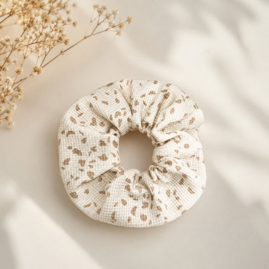 Chouchou d'allaitement upcyclé écru à taches beiges en coton gaufré, posé à plat avec des fleurs séchées