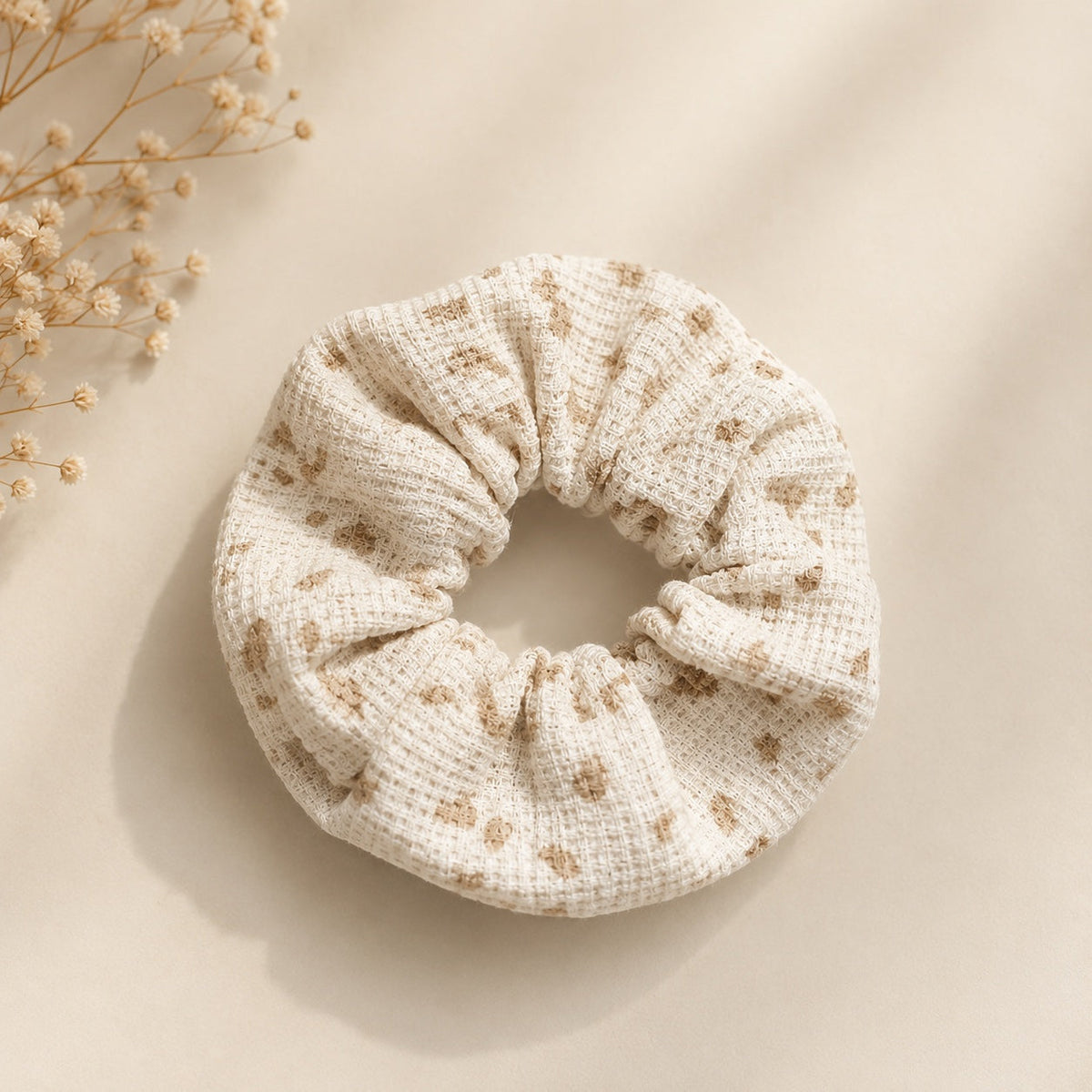 Petit chouchou enfant upcyclé écru à taches beiges en coton gaufré, posé à plat avec des fleurs séchées