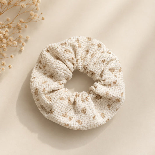 Petit chouchou enfant upcyclé écru à taches beiges en coton gaufré, posé à plat avec des fleurs séchées
